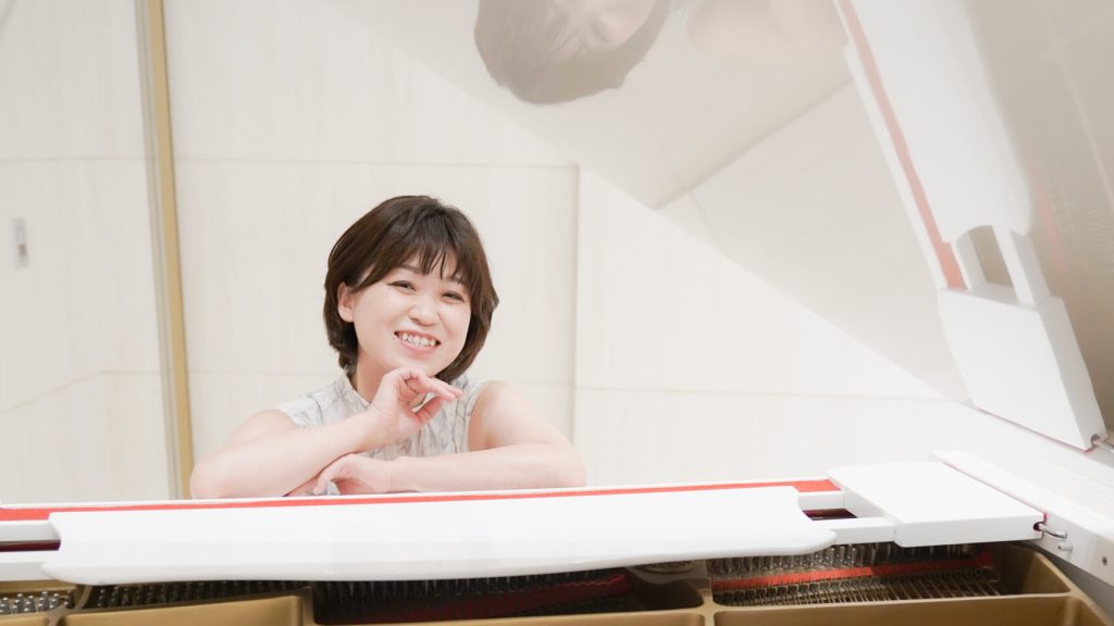 グランドピアノの前で微笑むKONOMIさん